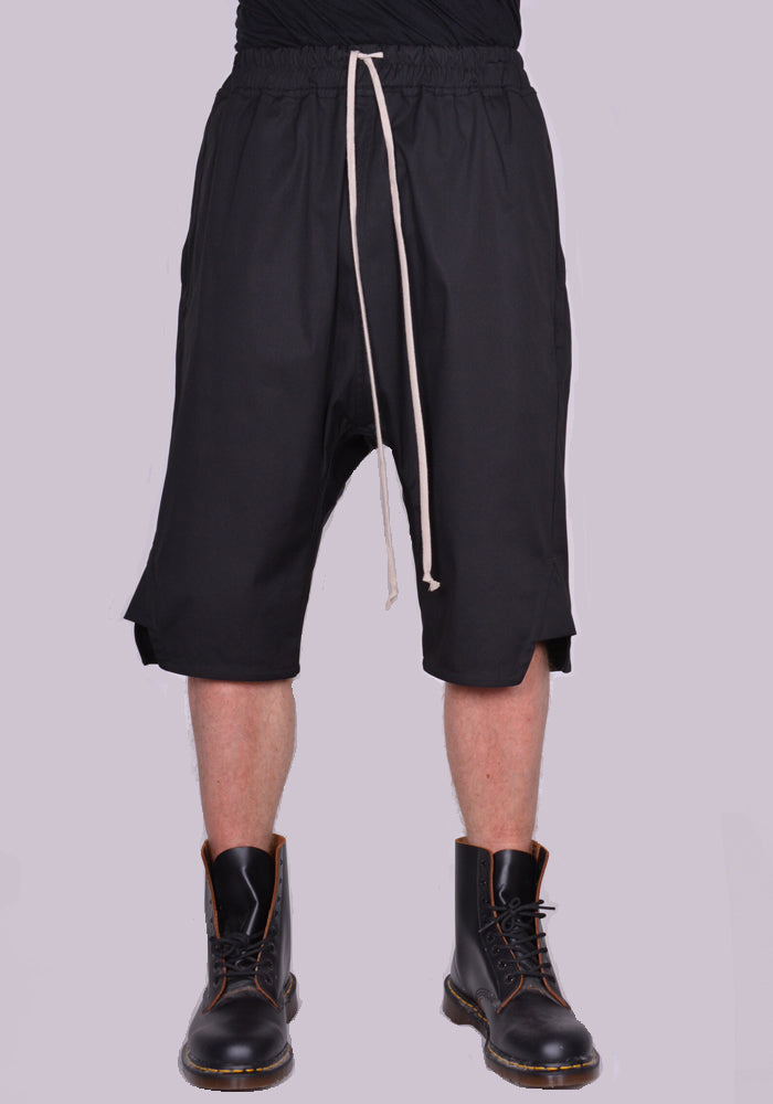 Men's short pants in black cotton featuring an elastic waist band with a drawstring closure, a drop crotch and side slit hem